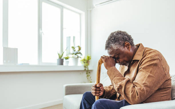 Thoughtful elderly man sitting alone at home with his walking cane